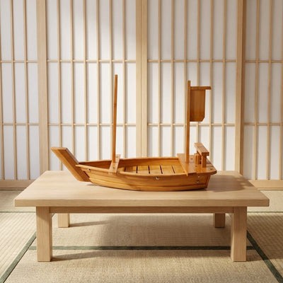 Boat sushi wood natural bamboo construction with tall sail mast on blonde wood coffee table near lattice screen