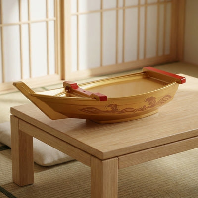 Boat sushi golden finish with engraved wave pattern and red dividers on wooden coffee table near shoji screen