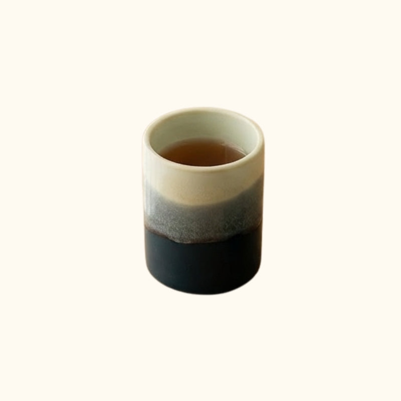 Ceramic japanese tea cup with ocean gradient glaze from ivory to deep blue filled with tea on white background