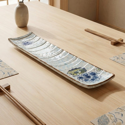 Handcrafted ceramic sushi plate with blue chrysanthemum motifs and wave texture on minimalist Japanese dining table