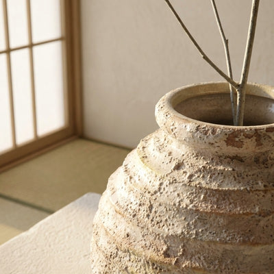 Close up of handmade ceramic vase ikebana showcasing rough striped texture with branches near shoji screen