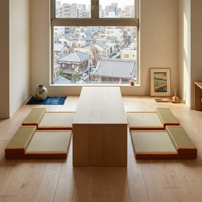 Japanese orange floor cushion set with beige tatami surfaces around wooden table near window with temple rooftops view and ukiyo-e print