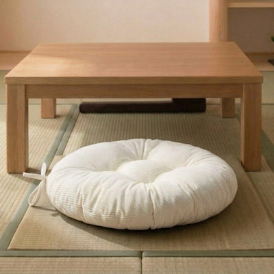 Placed in front of a low wooden table on tatami mats, this cushion for meditation in white color has a ribbon tie