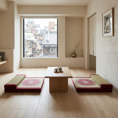 Meditation floor cushion pair with burgundy borders chrysanthemum motifs beside wooden table near window with traditional rooftops view