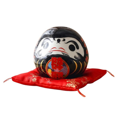 Guardian daruma doll japanese black with vibrant red details displayed on ceremonial red silk cushion against clean white background for clear product view