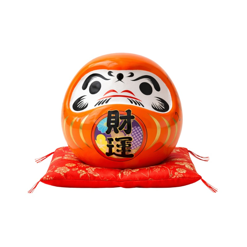 Entrepreneurial daruma japanese ceramic in glossy orange finish with colorful kanji details displayed on red floral cushion against clean white background