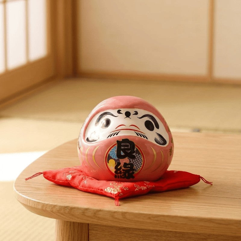 Tender daruma pink japanese in blush tones with love characters resting on red silk cushion atop round wooden table in peaceful tatami floor setting