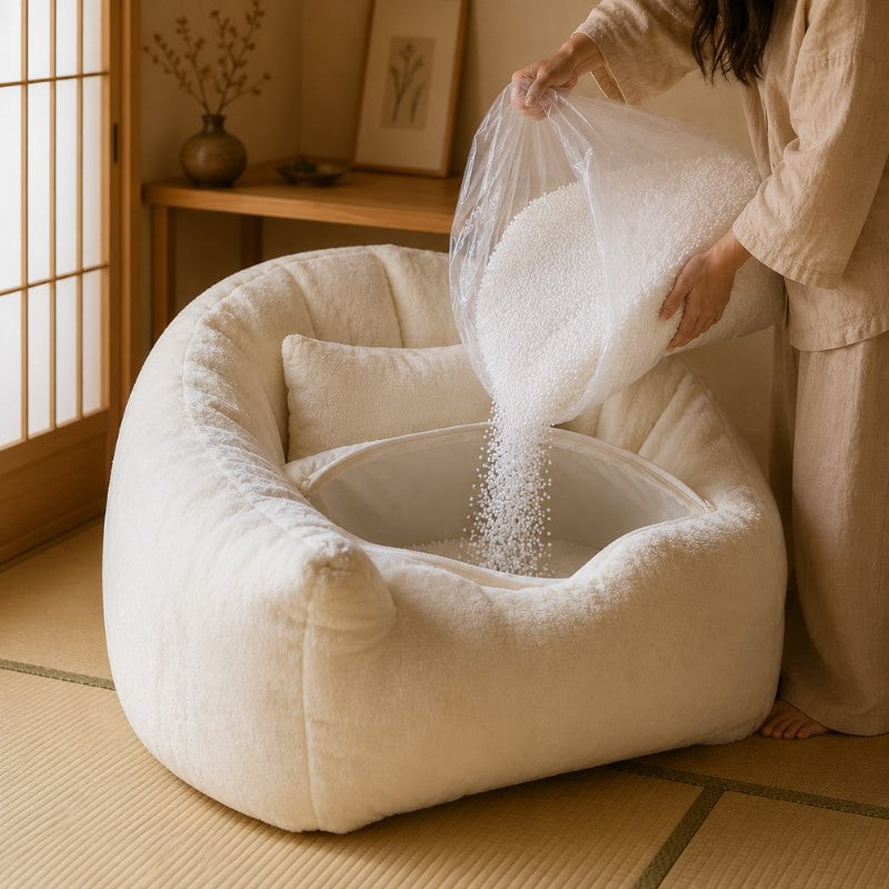 Woman filling white teddy fleece bean bag chair with white micro bead filler poured from transparent bag in warm Japanese minimalist interior