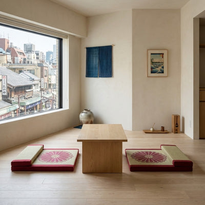 Floor cushion meditation set with burgundy fabric chrysanthemum designs flanking wooden table near window with urban view noren and ukiyo-e art