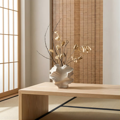 Sculptural floral japanese vase with organic wavy form and dried botanical arrangement near bamboo blind