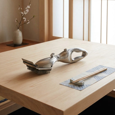 Elegant grill bbq brush with sculpted metallic handle on Japanese dining table with chopsticks on hashioki rest and cherry blossom vase in sunlit room