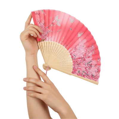 Graceful hands displaying hand japanese fan featuring coral pink gradient with cherry blossom branches butterflies and carved bamboo ribs
