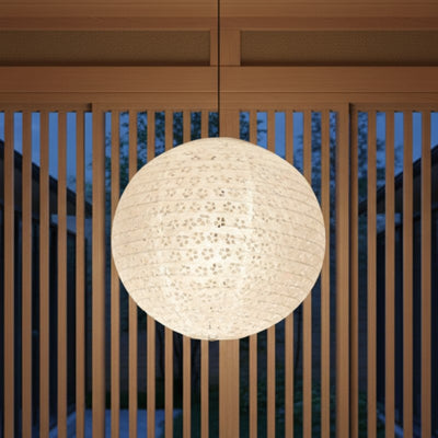 Round hanging japanese lantern glowing softly beneath wooden beam railing overlooking serene outdoor garden area