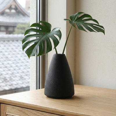 Modern ikebana vase flower arrangement featuring fresh monstera leaves by window overlooking japanese temple