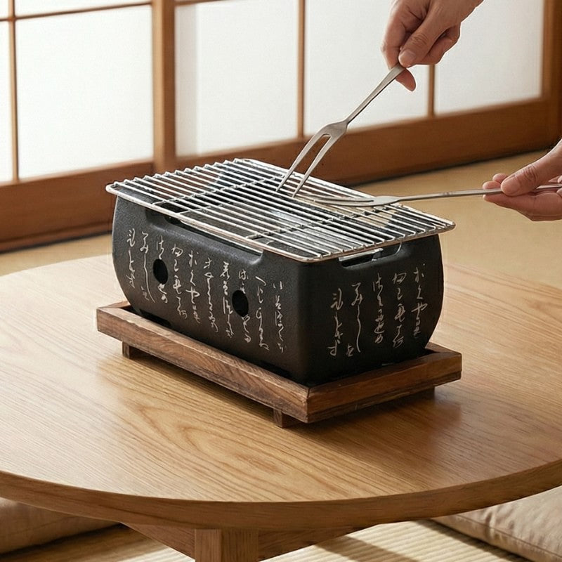 Japanese barbecue grill in use with metal tongs cooking food on ventilated charcoal burner, demonstrating traditional indoor grilling method