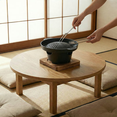 Japanese barbecue style cooking preparation with metal tongs over round ridged grill on low table with floor cushions