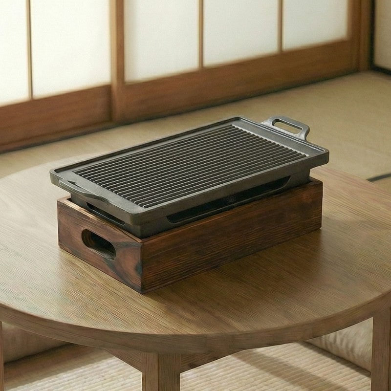 Japanese BBQ grill with elongated cast iron plate and natural wood charcoal box on round low table in authentic tatami setting