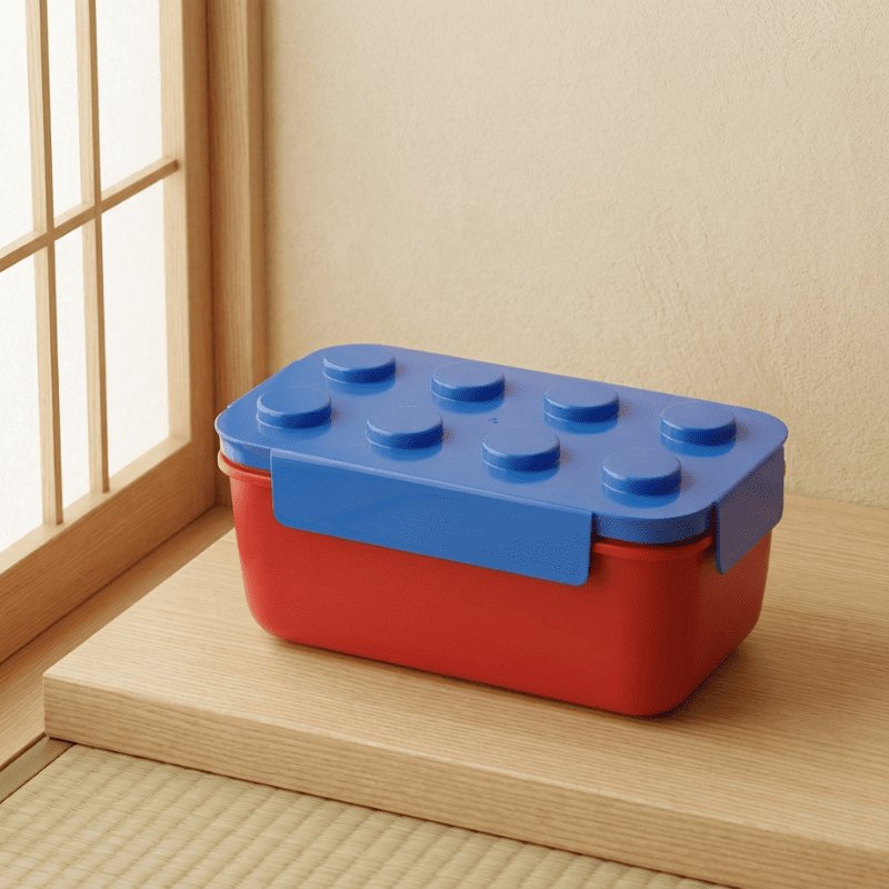 Cheerful japanese big bento snack box with red base and blue Lego top positioned on windowsill near traditional shoji screen in golden light