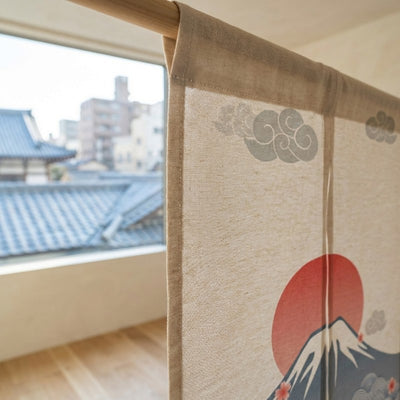 Close-up of japanese curtain noren texture showing Mount Fuji red sun and scrolling cloud motifs on natural linen fabric hanging on wooden rod with traditional Kyoto rooftop view