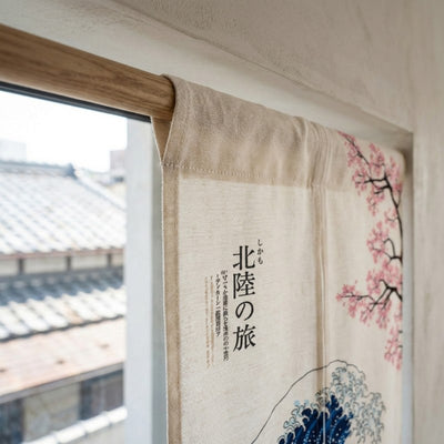 Close-up of japanese curtains noren texture showing Hokusai Great Wave cherry blossom and kanji calligraphy on natural linen fabric mounted on wooden rod with traditional rooftop view