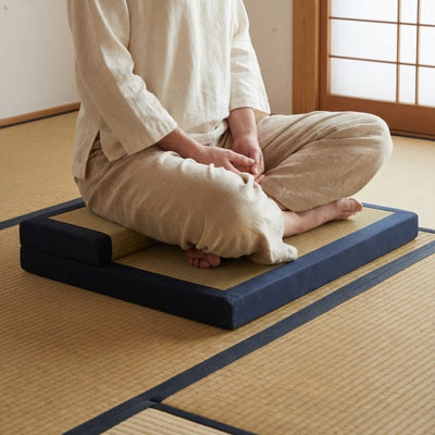 Japanese cushion with navy blue borders and person sitting seiza position in white clothing on tatami floor with shoji screen