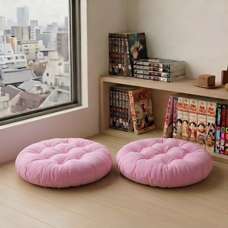 Two round pink cushions from the japanese cushions floor line sit on the wooden floor near a manga bookshelf