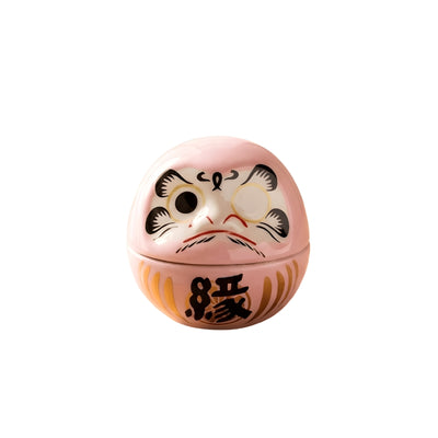 Japanese daruma doll pink featuring delicate coloring and black prosperity character with blank eyes on neutral backdrop