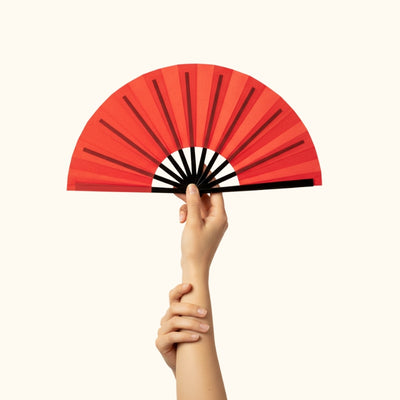 Elegant japanese fan red held gracefully in hand against white backdrop showcasing vibrant coral color and black wooden ribs