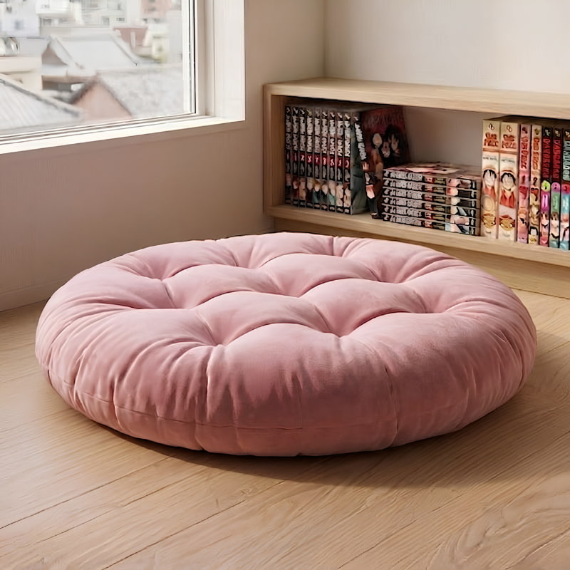 This tufted pink piece from the japanese floor cushions range rests near a bookshelf, bathed in window light