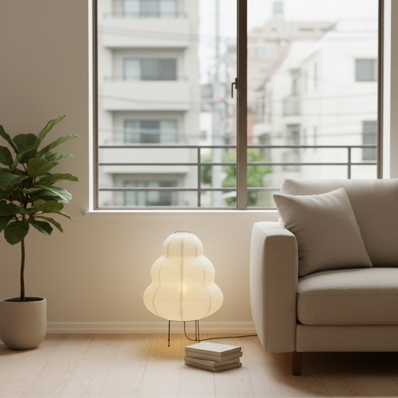 Japanese floor lamp paper rice shade with gourd shape and black wire tripod base next to beige sofa and fiddle leaf fig plant in minimalist living room