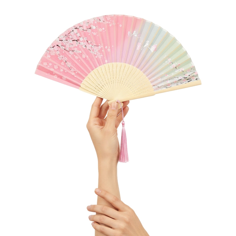 Traditional japanese hand fan pink with cherry blossom motif held delicately with both hands against minimalist white background highlighting artistic details