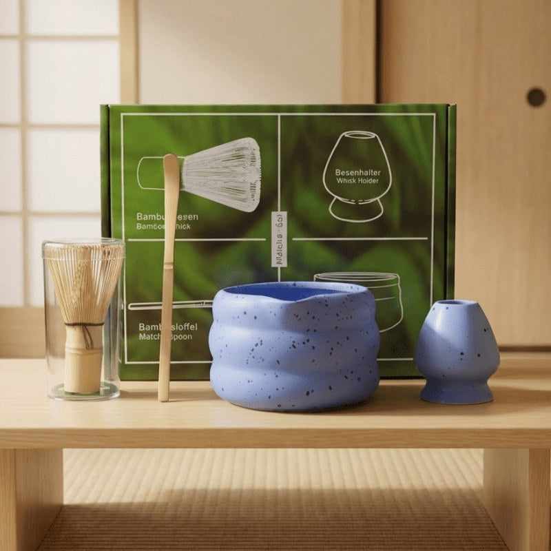 Blue ceramic matcha tea whisk set with bamboo accessories and green packaging arranged on wooden shelf beside shoji screen in natural light