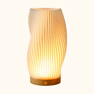 Japanese modern lamp white sculptural pleated shade with hourglass silhouette on natural wood base displayed on neutral background