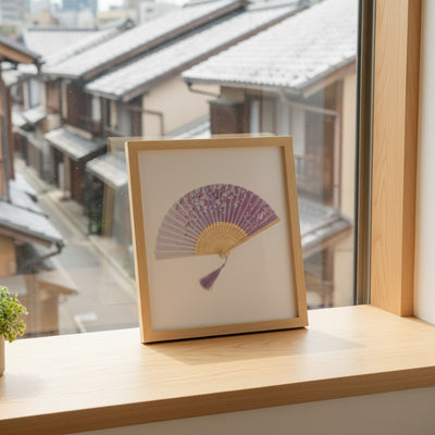 Framed japanese paper folding fan purple with scattered cherry blossoms displayed on wooden windowsill overlooking snowy traditional Japanese street