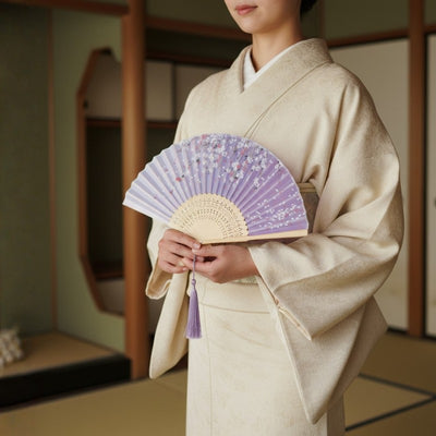 Graceful japanese paper folding fan in lavender displaying scattered cherry blossom pattern intricate bamboo carving and purple silk tassel