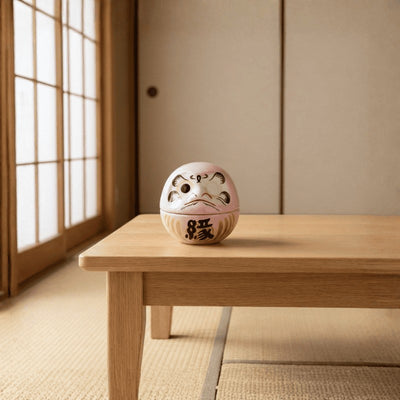 Japanese pink daruma doll with traditional facial design displayed on low wooden table beside shoji screen in serene tatami room