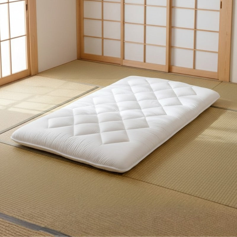 Japanese style futon with white quilted cotton and diamond stitching on tatami mat near shoji sliding doors