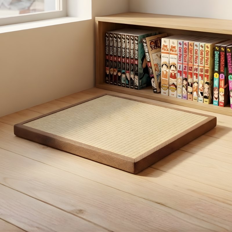 Japanese tatami mattress pad with woven rush surface and brown border near built-in bookshelf with manga collection