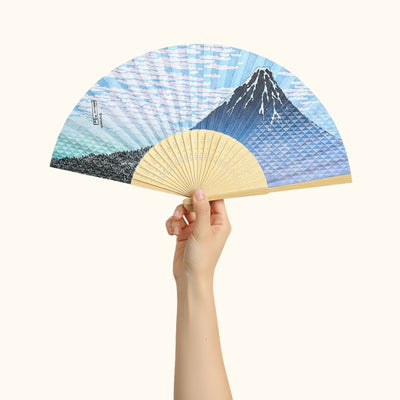 Elegant japanese traditional folding fan featuring Mount Fuji and ocean waves held gracefully against white backdrop showcasing detailed blue artwork
