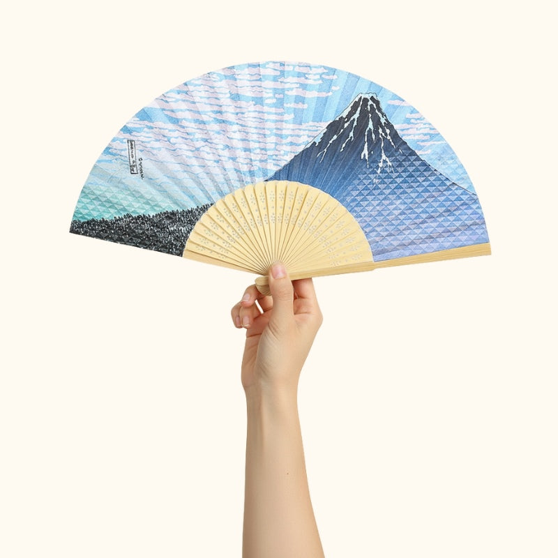 Elegant japanese traditional folding fan featuring Mount Fuji and ocean waves held gracefully against white backdrop showcasing detailed blue artwork