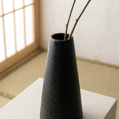 Handcrafted japanese vintage black vase with rough ceramic texture displaying branches on tatami mat flooring