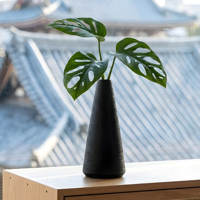 Textured japanese vintage vase holding monstera leaves on modern shelf overlooking traditional japanese rooftops