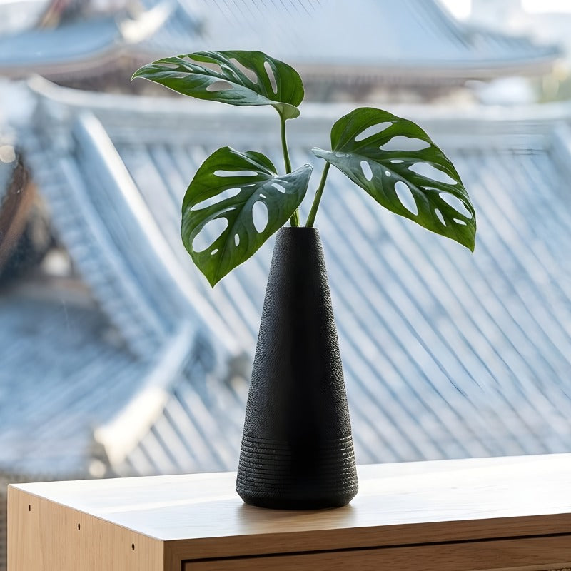 Textured japanese vintage vase holding monstera leaves on modern shelf overlooking traditional japanese rooftops