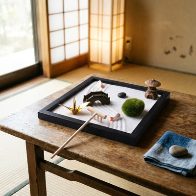 A black wood zen garden tray with raked white sand rests on a low wooden step between a tatami room and the corridor.