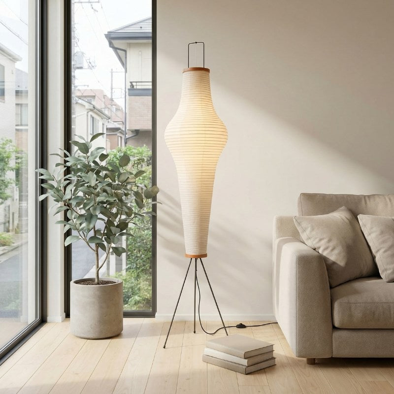 Elegant lamp akari with tall hourglass rice paper shade on minimalist tripod base near potted plant and window in contemporary Japanese interior