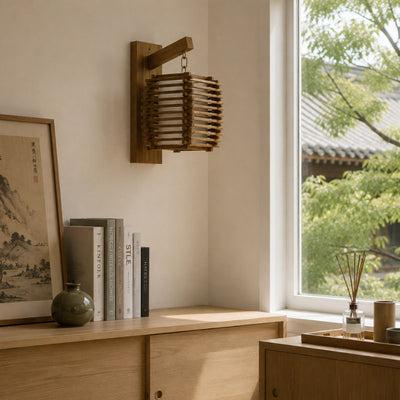 Slatted wood japanese wall lamp mounted above a light oak credenza with framed calligraphy art, stacked design books, and a round ceramic vase near a window overlooking a traditional tiled roof