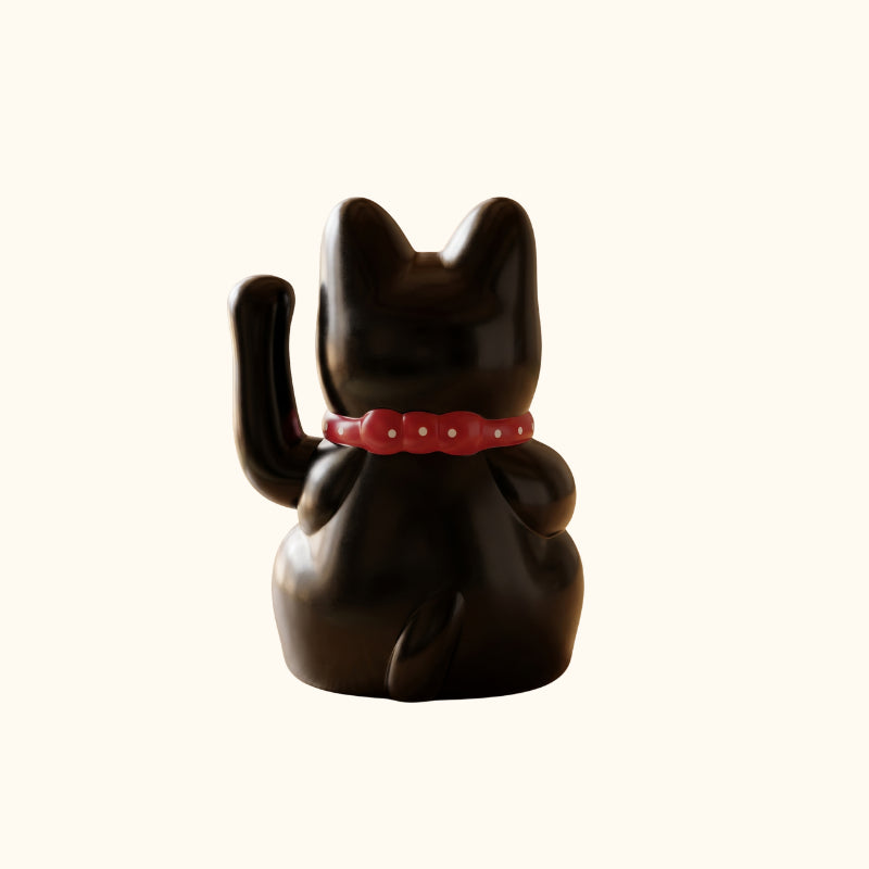 Rear view of a black lucky Maneki Neko cat statue with a raised paw, glossy finish and red collar.