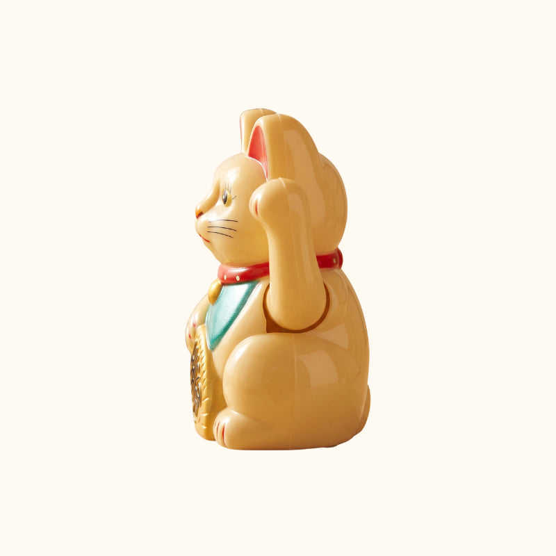 Side view of a golden Maneki Neko Japanese figurine with a raised paw, green bib and decorative gold coin.