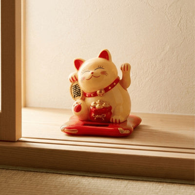 Traditional maneki neko yellow cat figurine with waving paw displayed on wooden windowsill catching soft afternoon sunlight