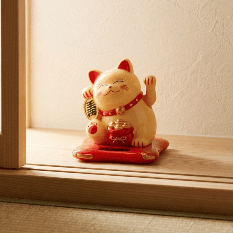 Traditional maneki neko yellow cat figurine with waving paw displayed on wooden windowsill catching soft afternoon sunlight